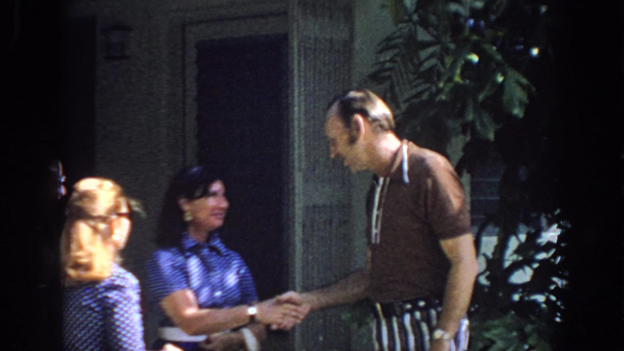 A 1972 Philadelphia home movie frame shows an older man shaking hands with a woman as another woman looks on near an outdoor entrance.