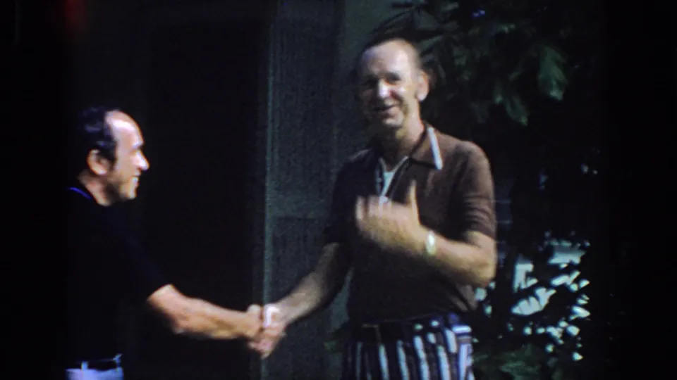The 1972 Philadelphia home movie shows two men shaking hands outdoors, with one man smiling toward the camera near the entrance.
