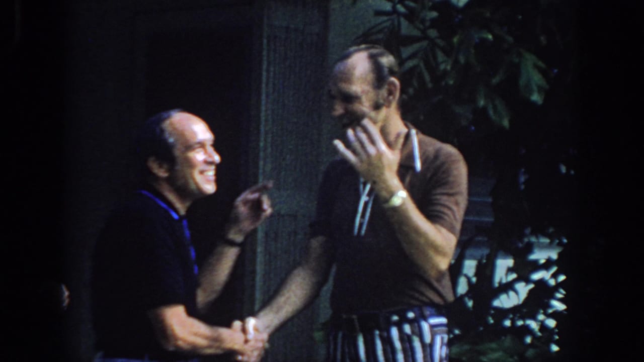 Two adult men in polo shirts share a smiling handshake outdoors in Philadelphia home-movie footage from 1972.