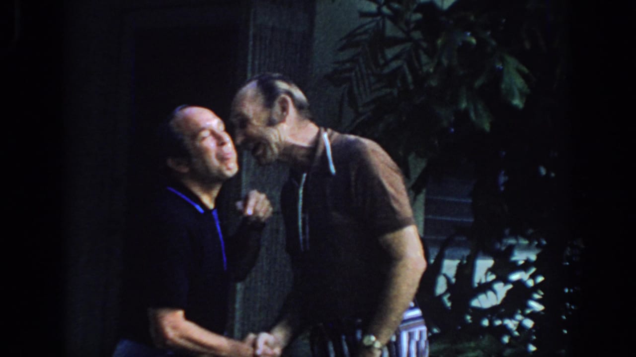 Two men lean close while laughing and shaking hands.