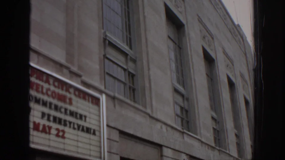 A tilted handheld view shows the Philadelphia Civic Center commencement marquee, tall windows, and stone facade.