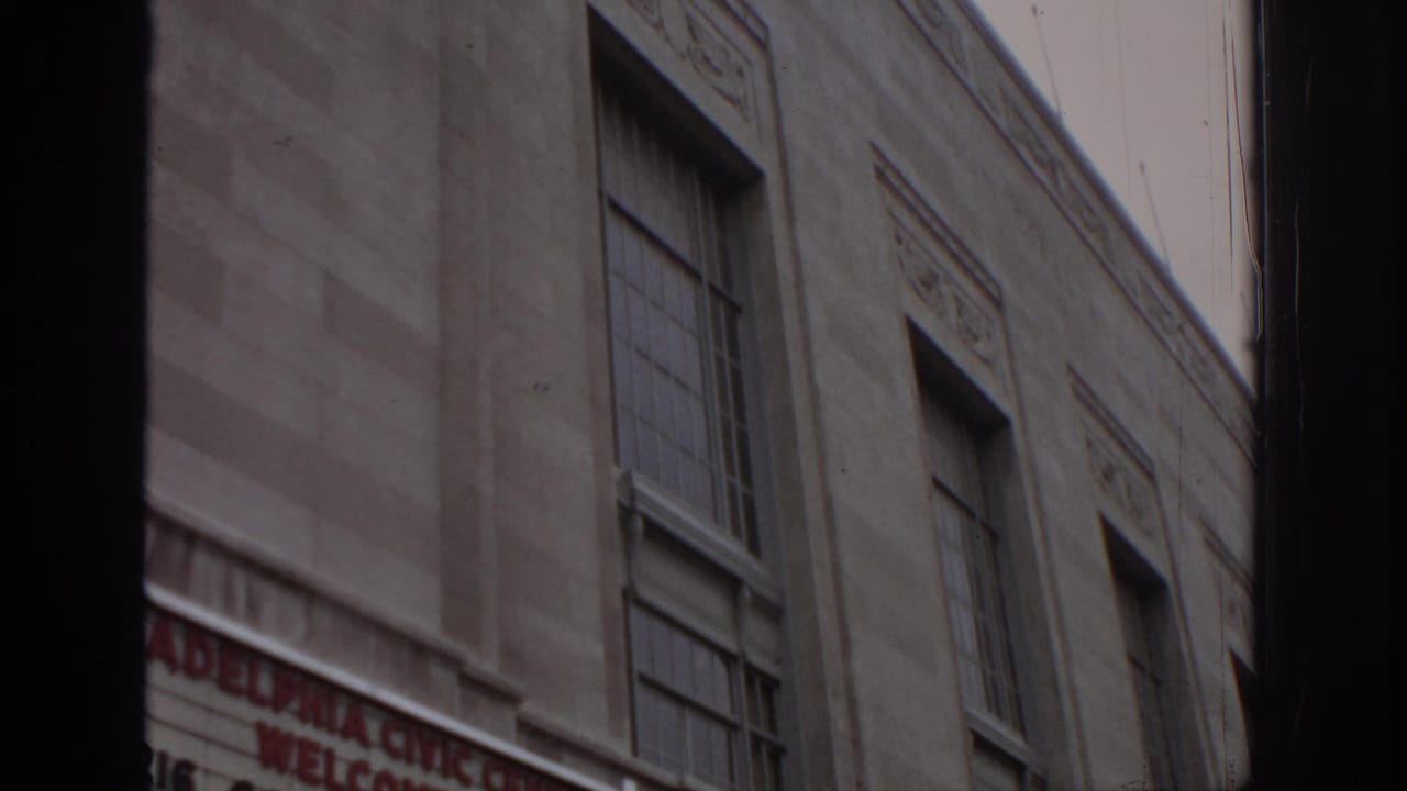 1972 Philadelphia home-movie frame showing a Civic Center exterior wall, tall windows, and a partially cropped welcome sign at street level.