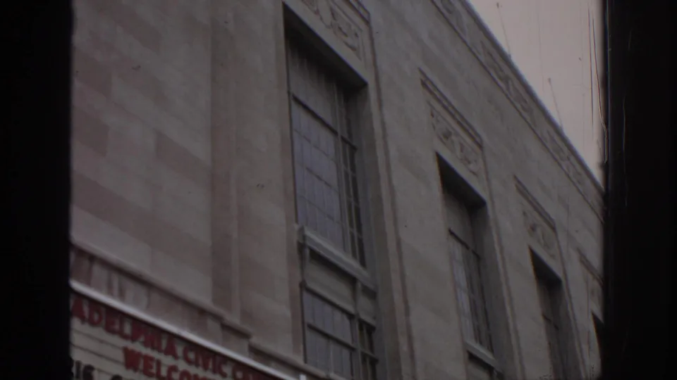 1972 Philadelphia home-movie frame showing a Civic Center exterior wall, tall windows, and a partially cropped welcome sign at street level.
