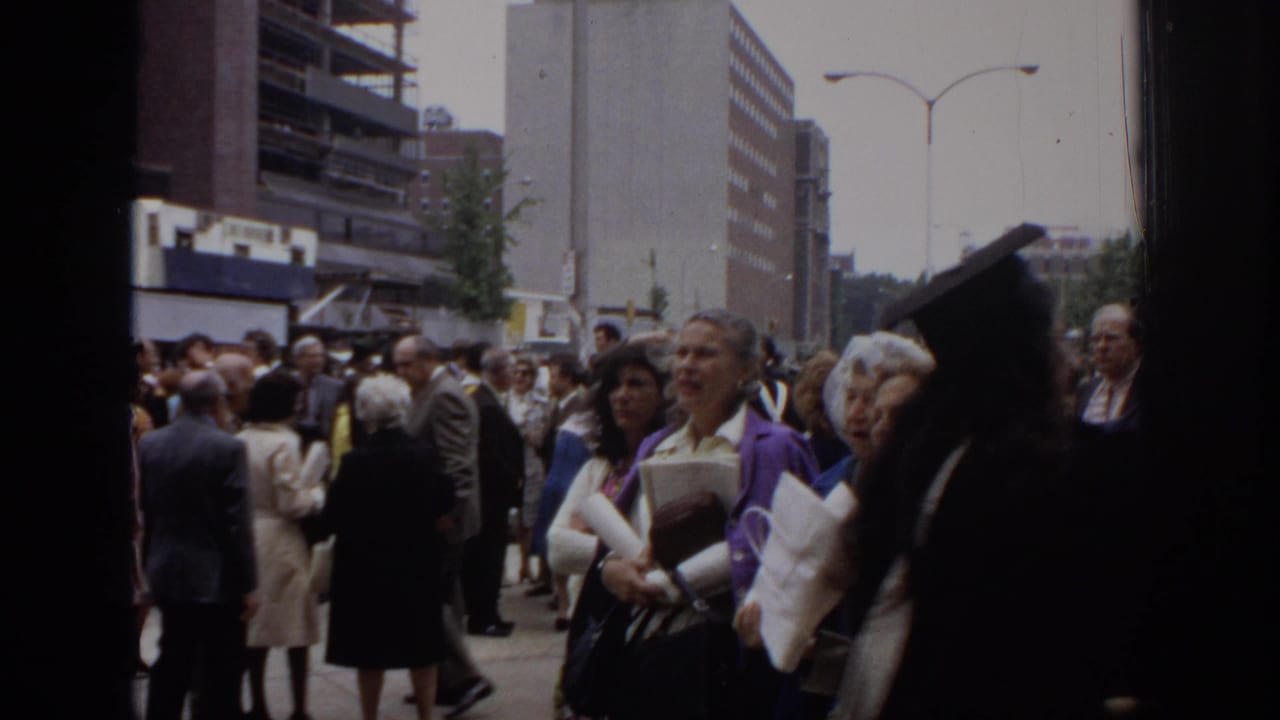 1972 Philadelphia frame of adults in suits, coats, and dresses gathered outside the Civic Center during a graduation-related crowd scene.