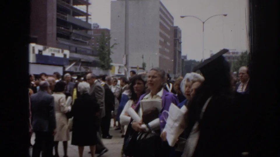 1972 Philadelphia frame of adults in suits, coats, and dresses gathered outside the Civic Center during a graduation-related crowd scene.