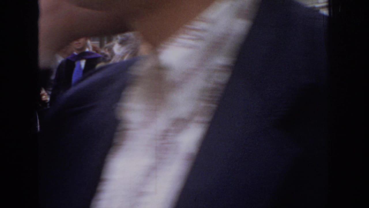 Close, blurred view of a person in dark clothing passing in front of the camera near a crowd.