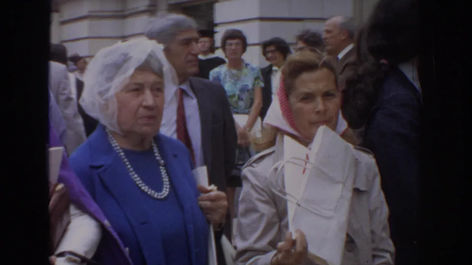 Close handheld 8mm view of a 1972 Philadelphia crowd with women in period attire, suited men, papers, and robe-like garments visible.