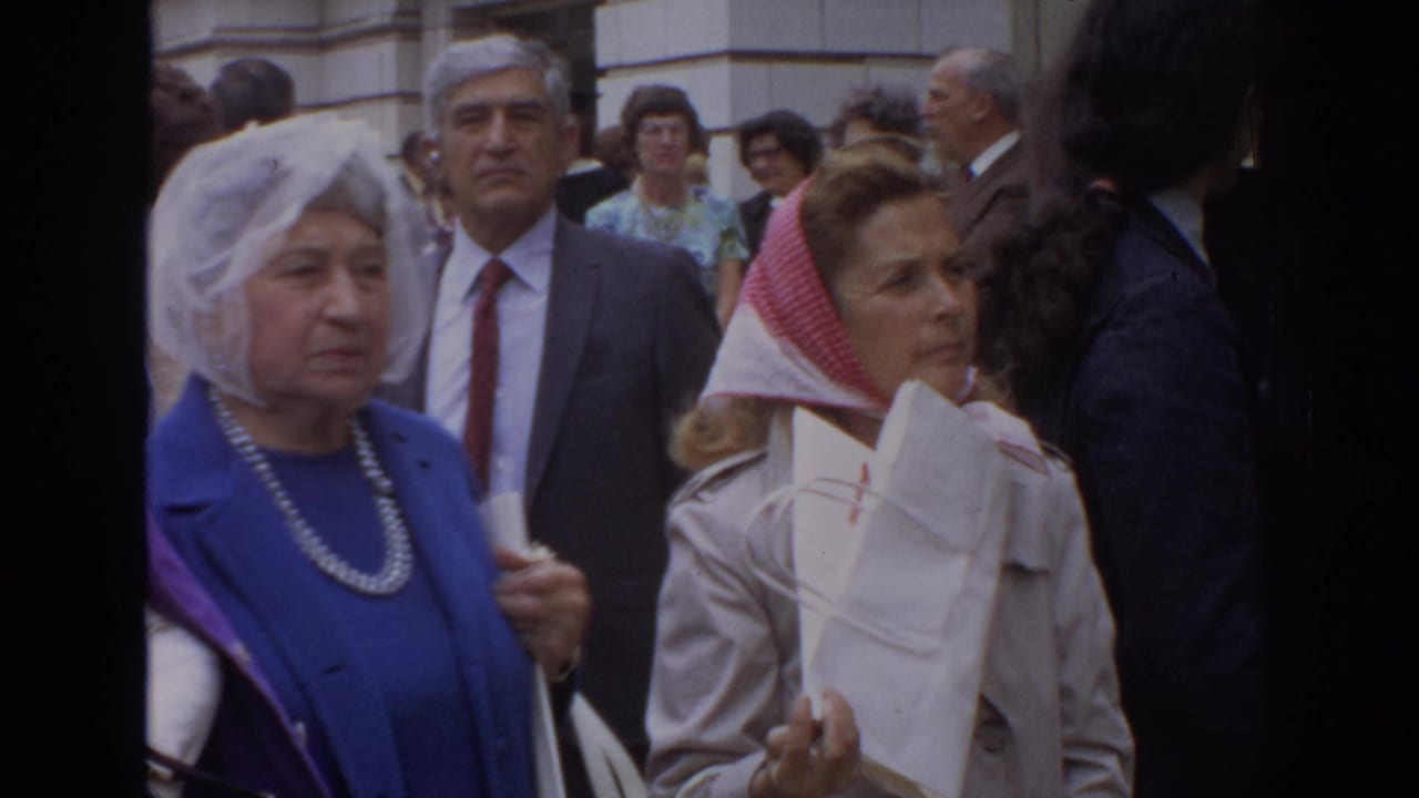 1972 Philadelphia home-movie frame showing older women and men in a close sidewalk crowd, including a woman in blue with pearls.