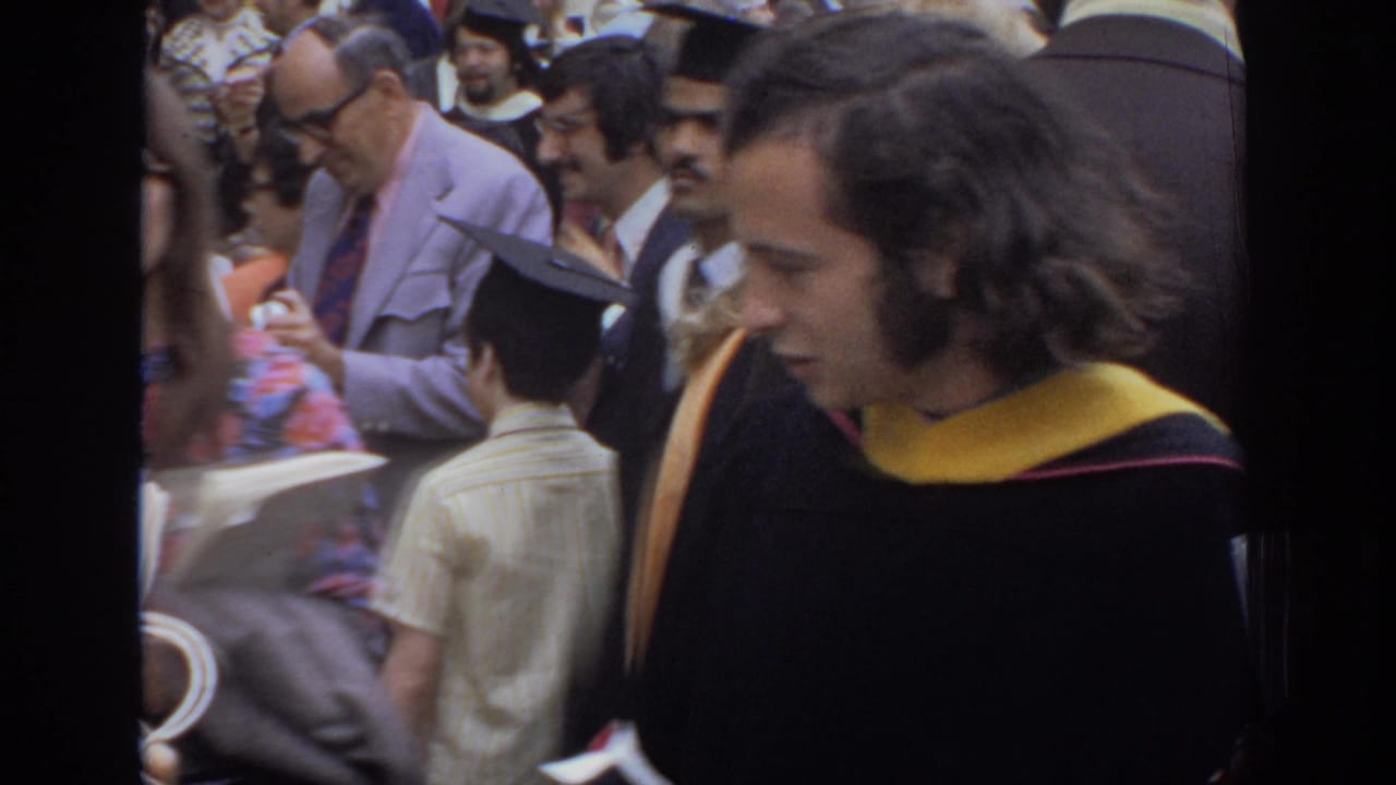 1972 Philadelphia graduation crowd with a young graduate in black gown and yellow hood near guests in suits and dresses.