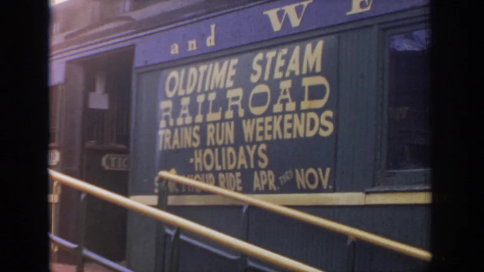 1972 8mm frame of the Black River railroad car sign, with platform railings cutting across the painted excursion notice.