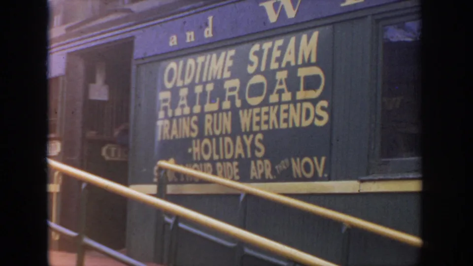 Soft 8mm view of the old time steam railroad sign on a dark railcar, with yellow platform rails in the foreground.