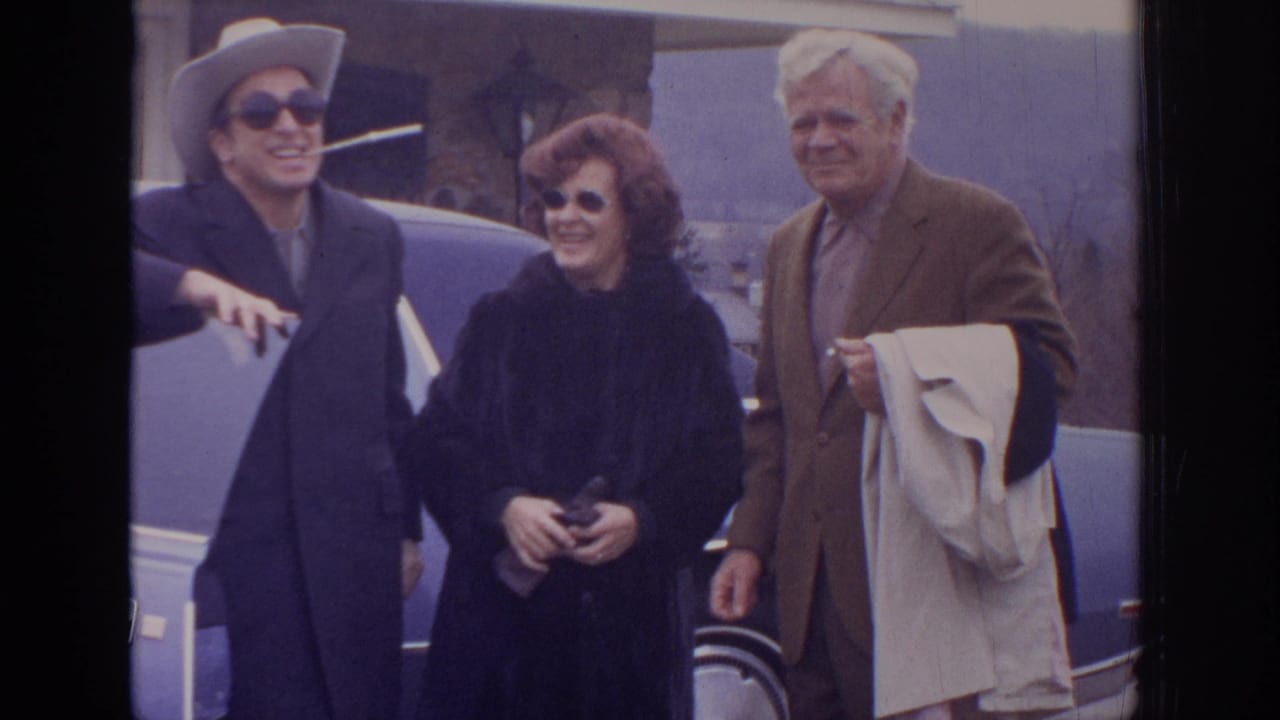 In 1972 home-movie footage, three adults stand near a blue sedan outside a stone building in Philadelphia, Pennsylvania.