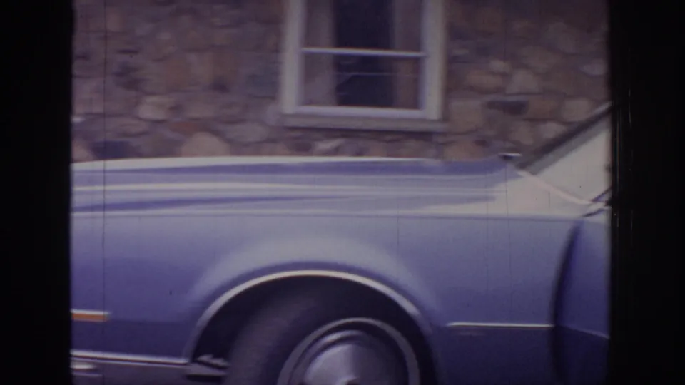Soft 8mm frame showing the side panel and wheel of a blue sedan outside the same stone building.