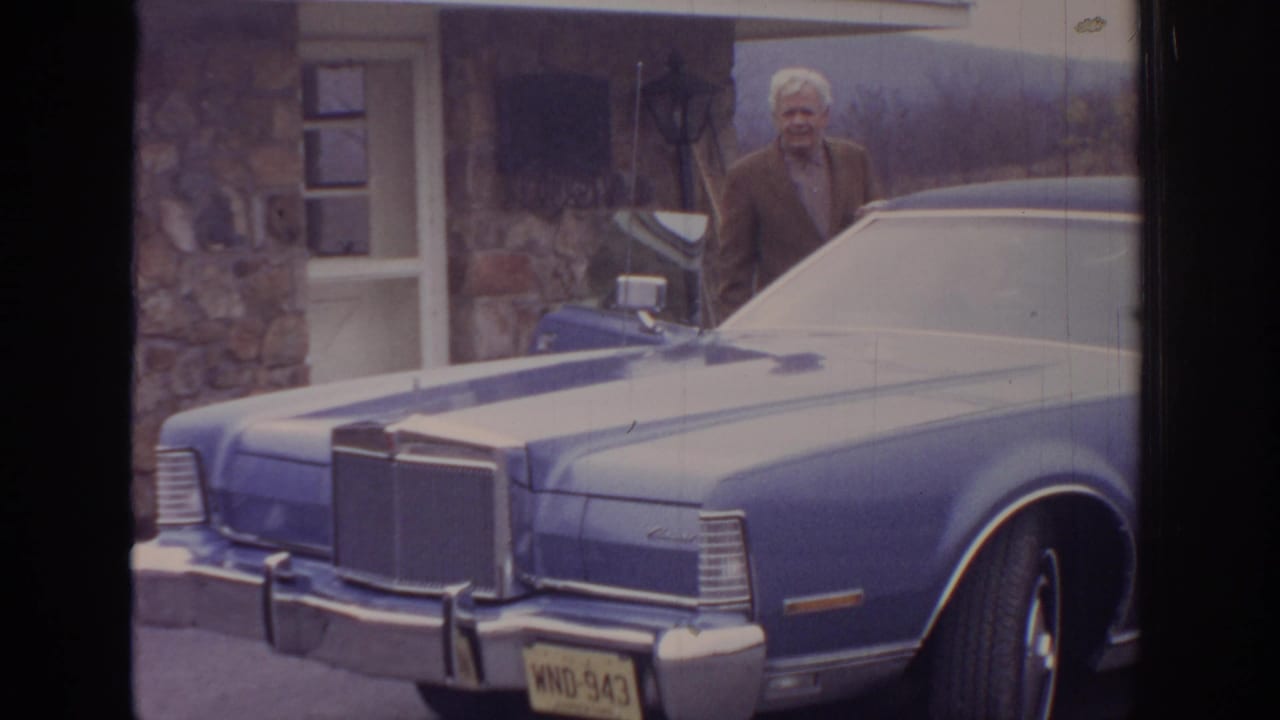 1972 Pennsylvania Super 8 frame showing an older man near a blue classic sedan parked by a stone house.