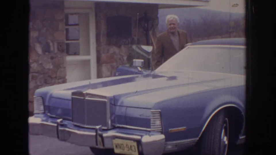 1972 Pennsylvania Super 8 frame showing an older man near a blue classic sedan parked by a stone house.