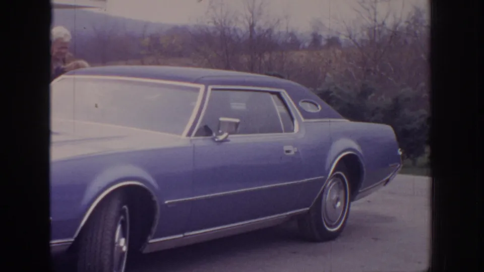 Super 8 frame of a blue 1970s sedan in side view, parked near a home exterior in Pennsylvania.