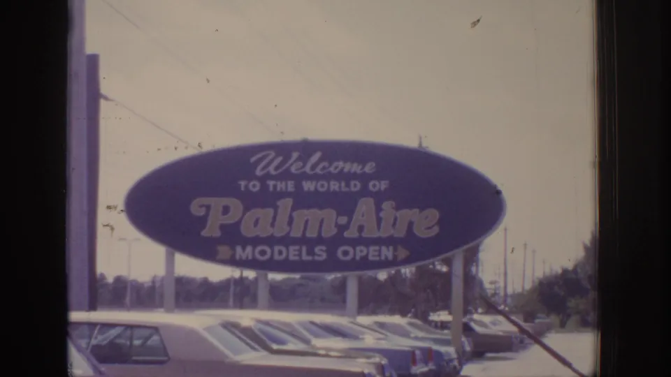 1970s 8mm frame showing a legible Palm-Aire welcome sign with parked cars below, likely from the same travel home movie.
