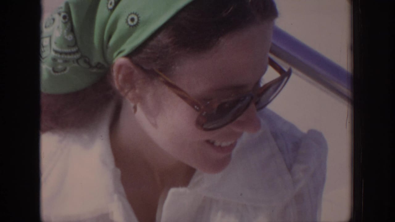 Woman in sunglasses smiles while looking down near a car window.