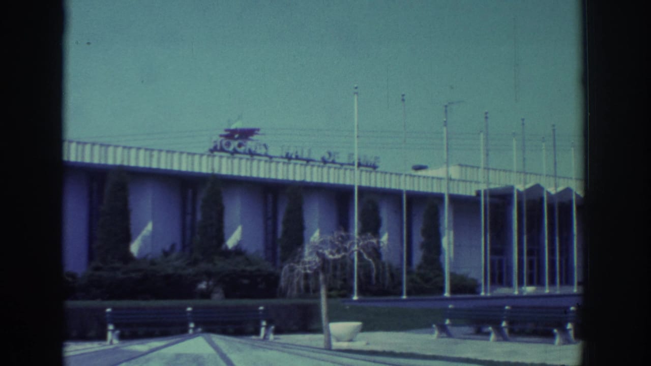 1972 Toronto 8mm frame showing the Hockey Hall of Fame exterior with flagpoles, benches, shrubs and a clear sky.