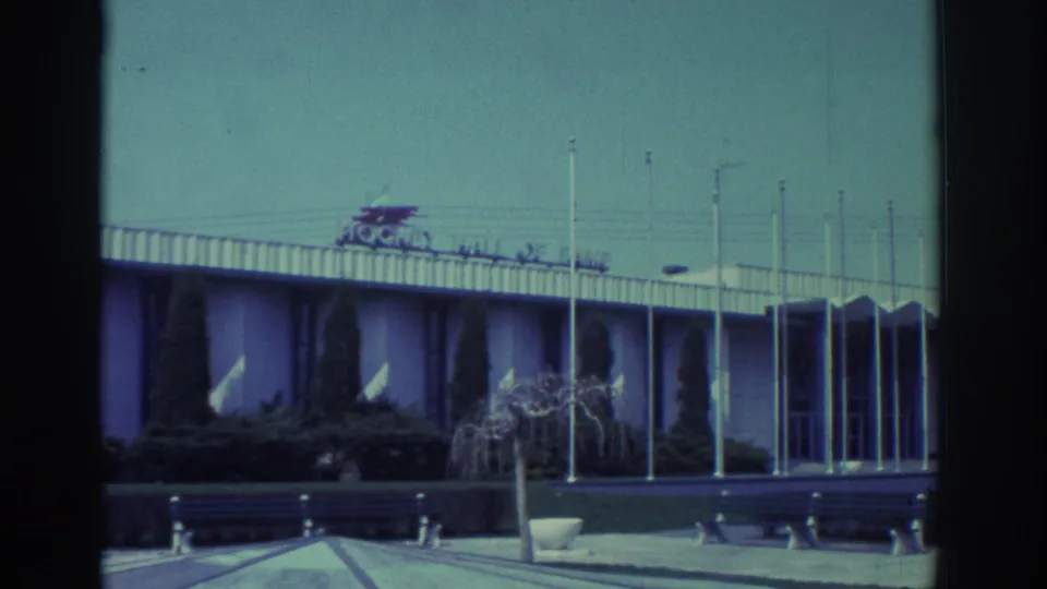 1972 Toronto 8mm frame showing the Hockey Hall of Fame exterior with flagpoles, benches, shrubs and a clear sky.