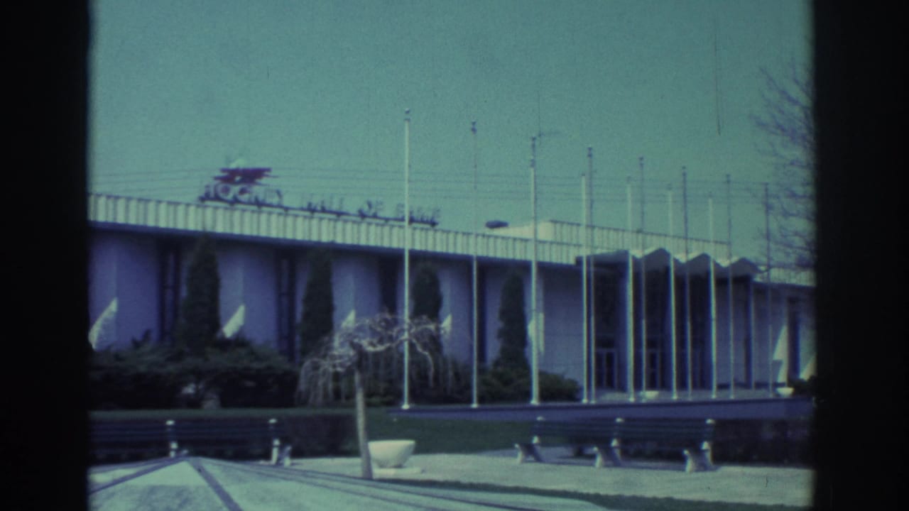 Exterior building facade with flagpoles, benches, shrubs and a roofline sign.