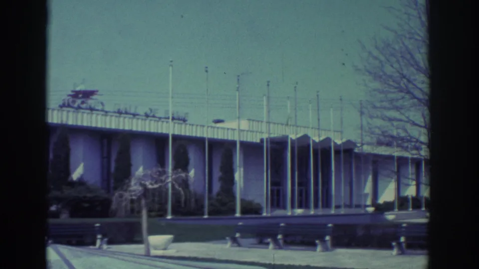 1972 Toronto exterior view of the Hockey Hall of Fame building, showing flagpoles, landscaping, benches and bare branches at frame edge.