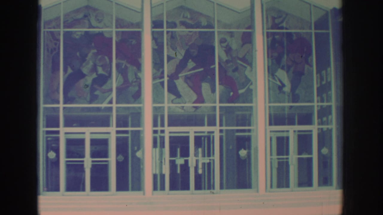 White-framed glass building facade with colorful stained glass figure panels above entrance doors.