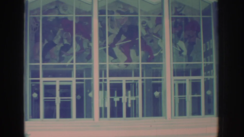 Close 1972 Toronto home-movie view of stained glass figures and entrance doors within a modern white mullion grid.