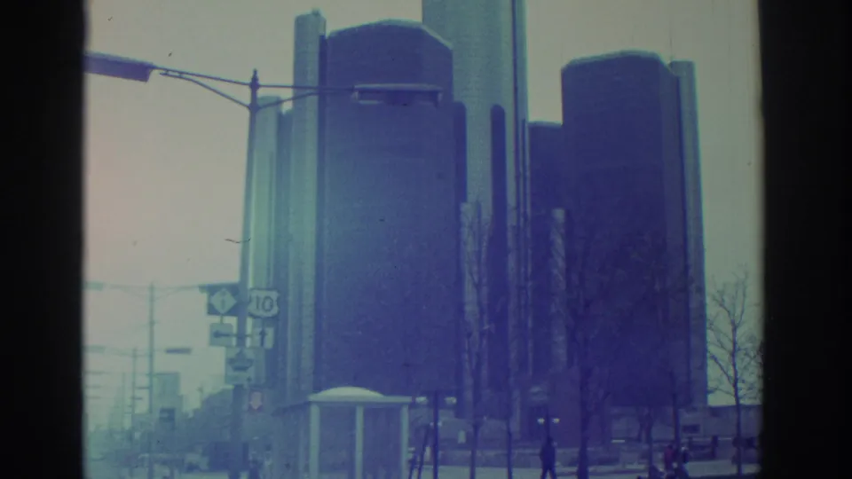 1972 Toronto street view with high-rise towers, a road sign, streetlight arm, bare trees, and distant pedestrians near the curb.