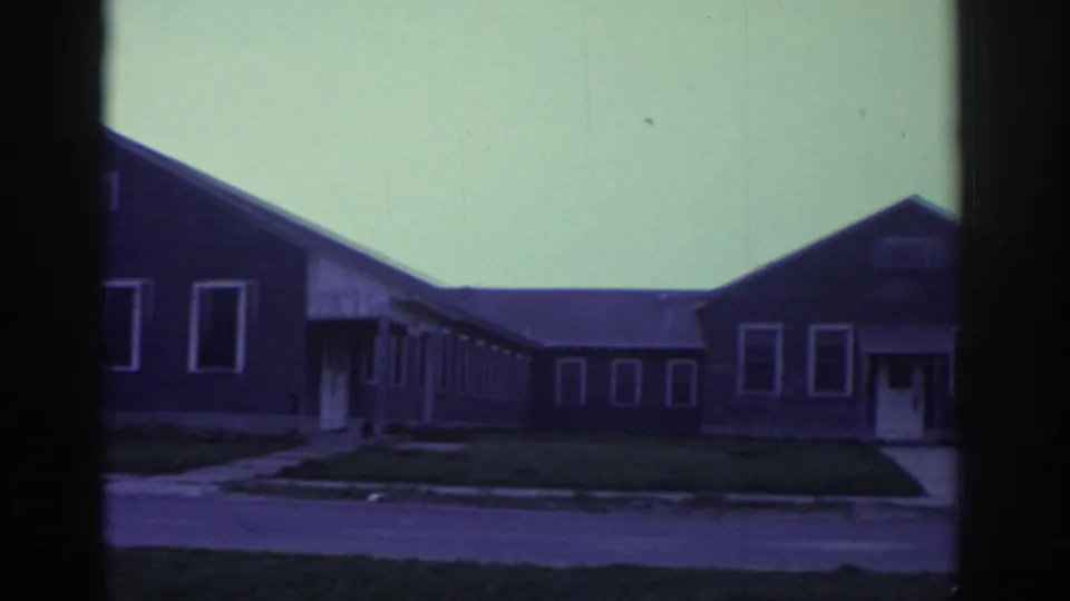 The pan continues across the Toronto exterior, with a long low facade, repeated windows, grass, sidewalk, and road visible.