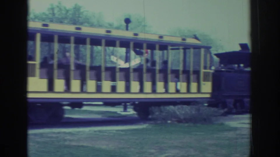 1972 Toronto home-movie frame centered on an open yellow sightseeing rail car with passengers seated behind vertical posts.