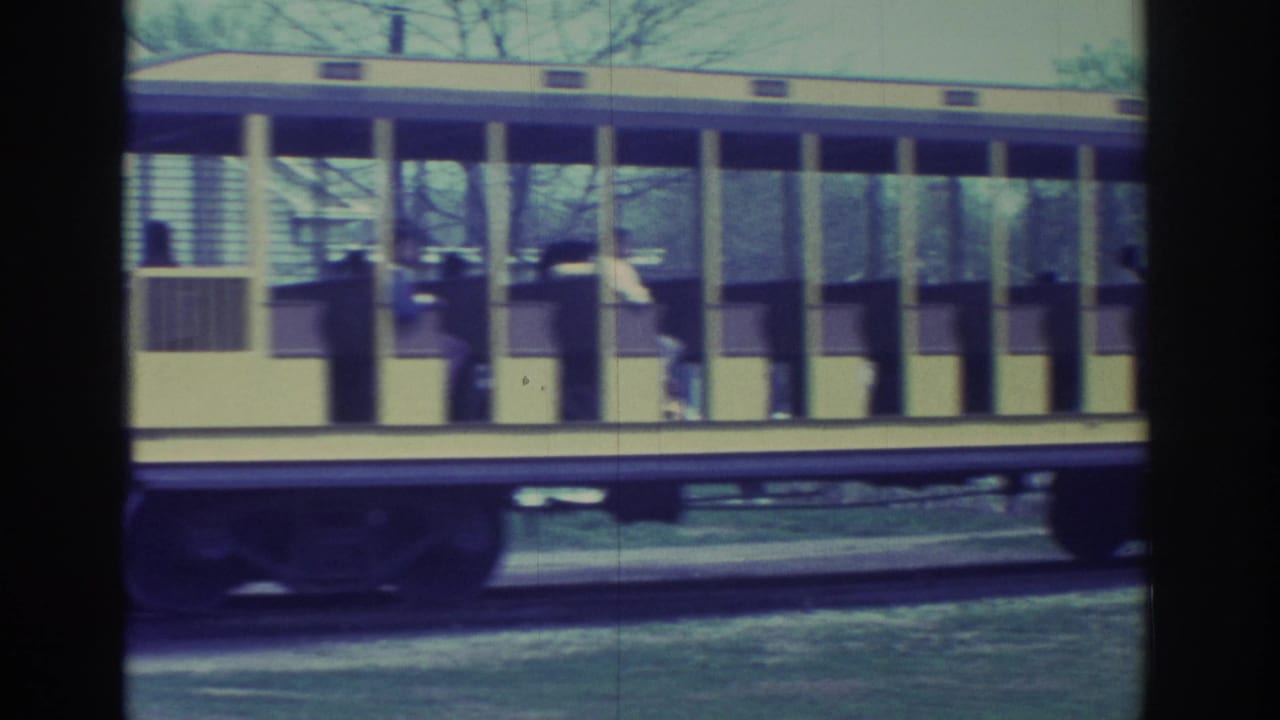 1972 Toronto home-movie frame showing a yellow and purple open-sided tram with seated passengers moving past the camera.