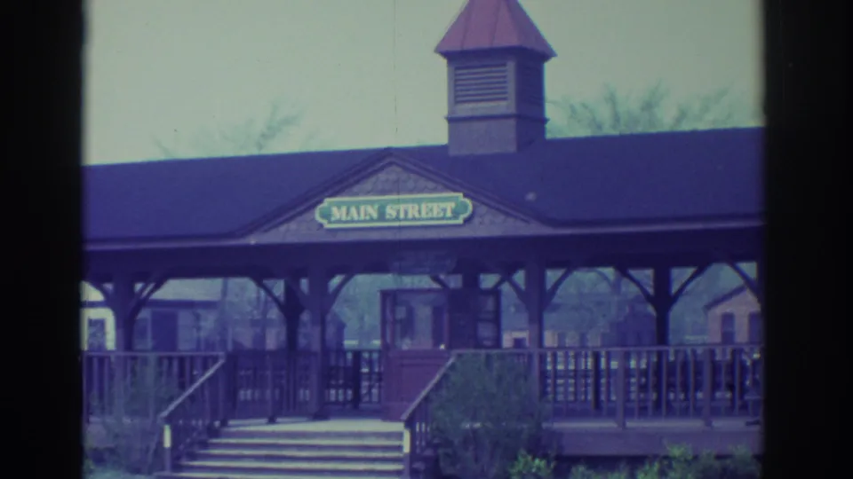 Wooden Main Street station at the amusement setting, with sign, platform railings, stairs, and faded 8mm color.
