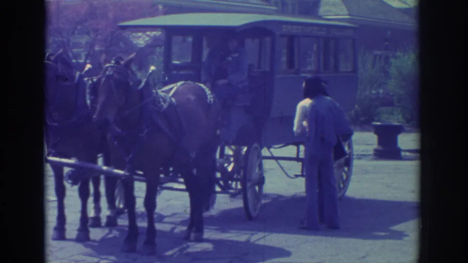 The carriage appears marked Greenfield Village, with two horses at front and a man standing beside the rear wheel in faded 8mm color.