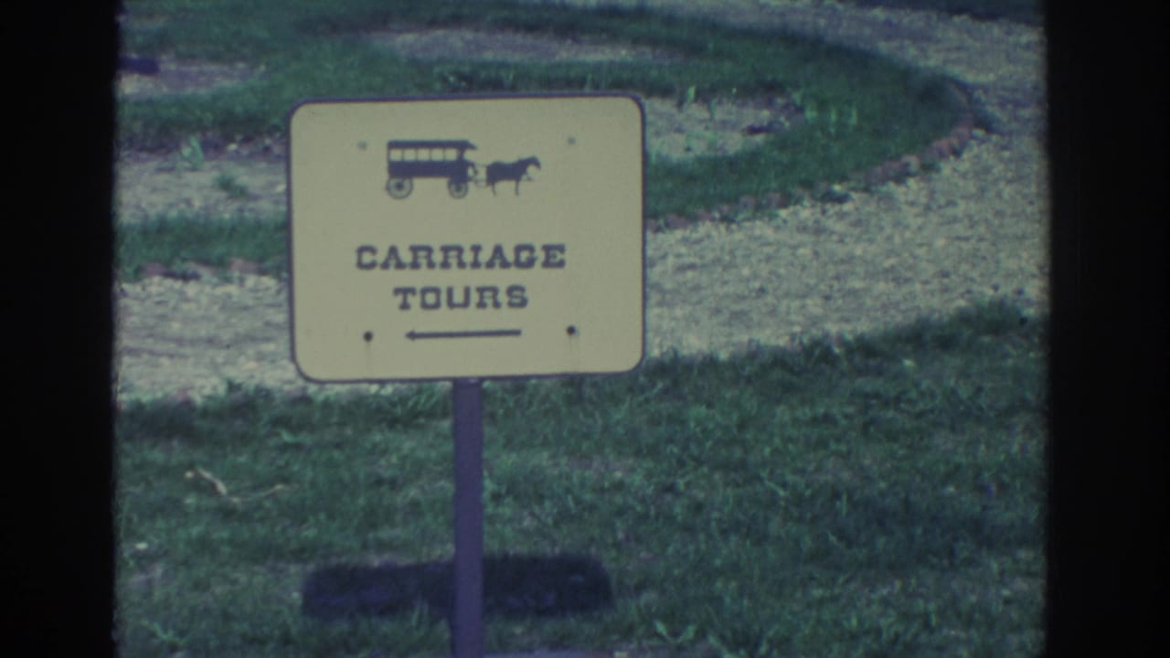 Yellow Carriage Tours sign with horse-drawn wagon icon standing on grass.