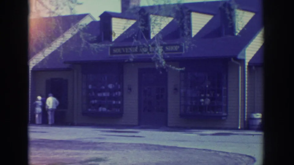 1972 Toronto home-movie frame showing a small souvenir and book shop with dormer windows and two people outside near the storefront.
