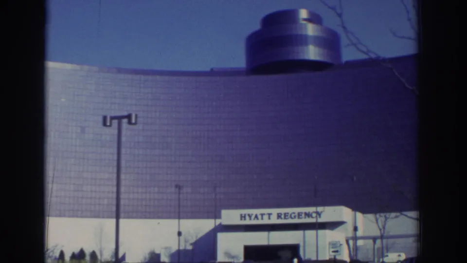 1972 Toronto Hyatt Regency exterior showing the upper facade, cylindrical rooftop element, entrance sign, bare branches, and a vehicle at frame edge.