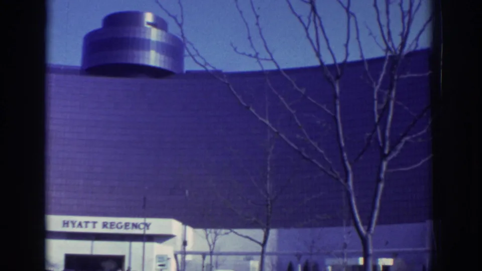 1972 Toronto hotel exterior with bare branches in the foreground, curved glass facade, and partial Hyatt Regency sign.