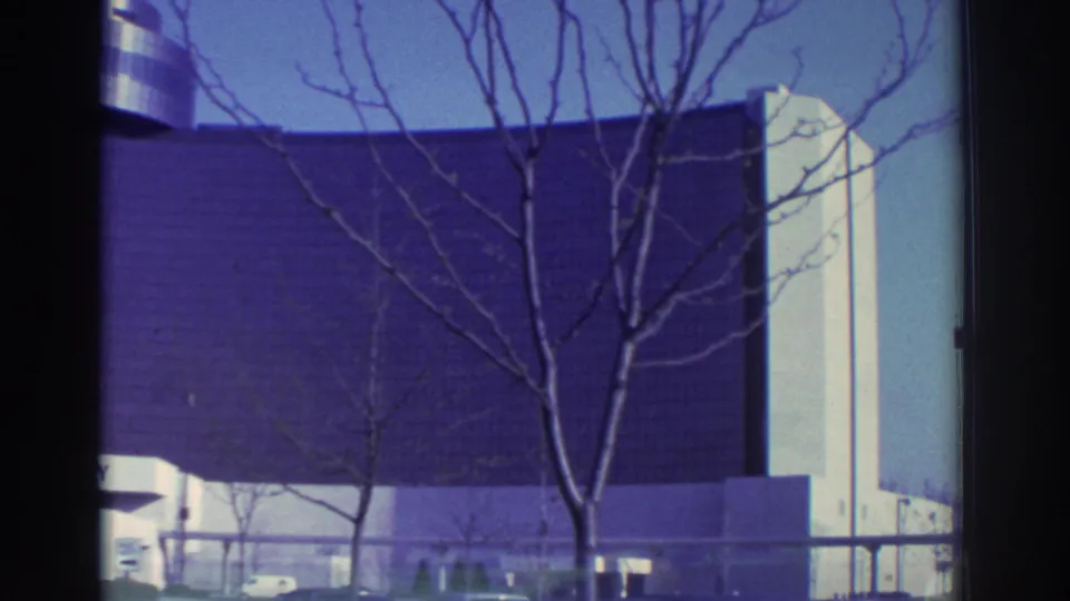 1972 Toronto home-movie frame showing a modern building facade, leafless branches, and part of an elevated transit structure.