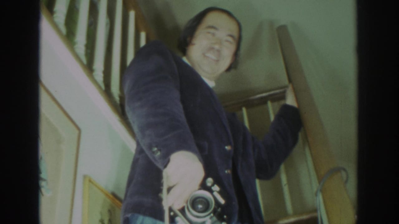 Man smiling from a staircase while holding a camera near his side.