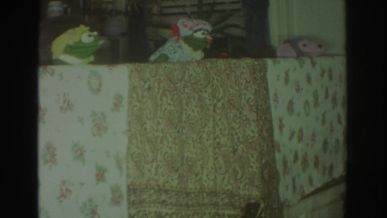 1972 Toronto 8mm frame showing frog and bird-like puppets above floral and paisley fabric stage panels.