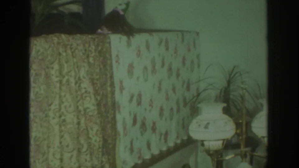 1972 Toronto 8mm frame holding on the puppet stage, with patterned fabrics, a dark puppet, and a lamp at right.