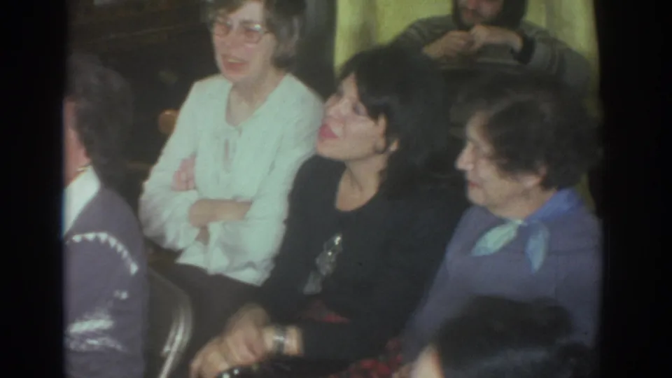 Toronto 1972 home-movie frame showing adults seated closely indoors, with faces turned toward activity off camera.