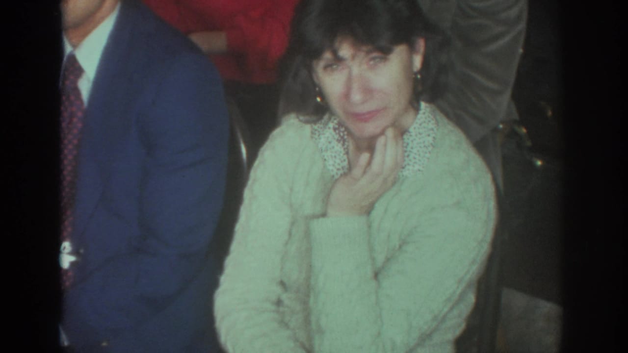 Woman in a pale sweater sits among adults at an indoor gathering.