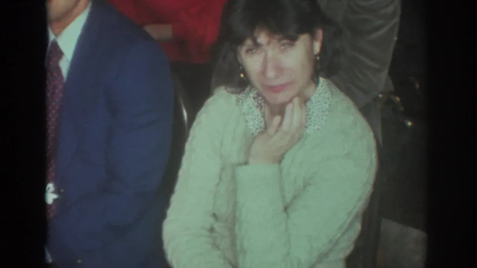 In a Toronto 1972 home-movie frame, a woman in a pale green sweater sits close to the camera among adults in a living room.