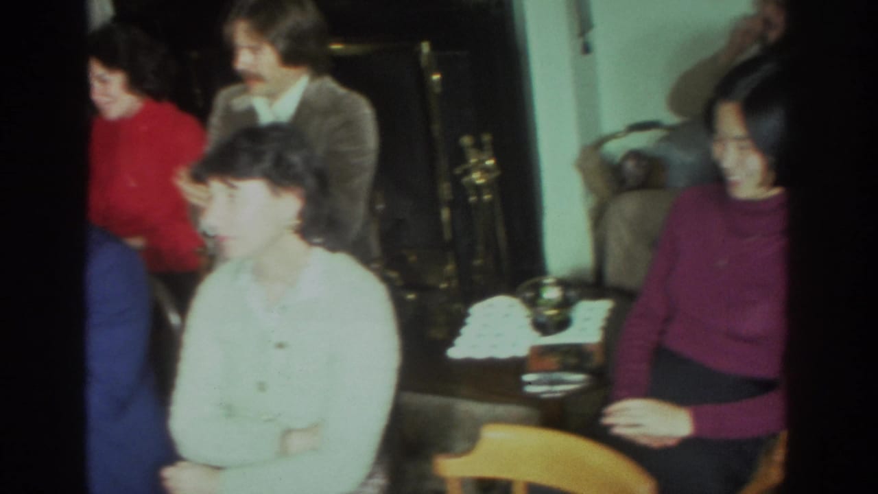 Adults seated in a living room, with some faces blurred by motion and a fireplace area in the background.