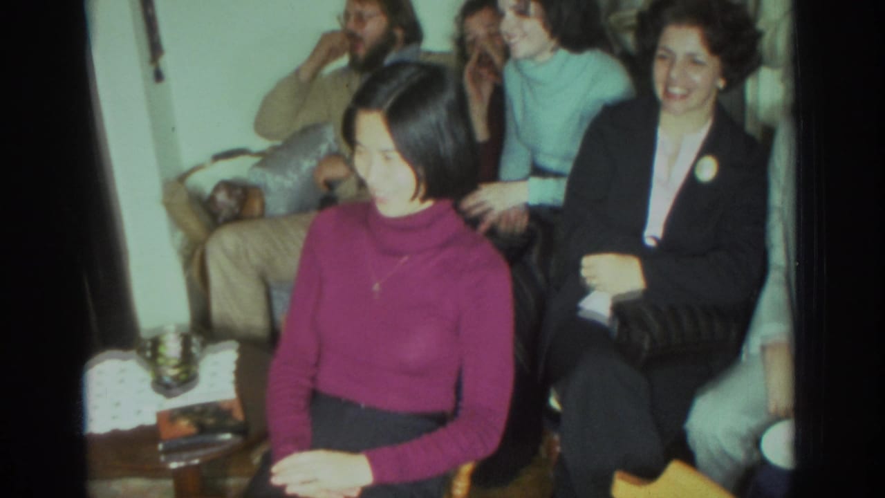 Several adults sit close together, including a woman in a magenta turtleneck and a woman in a dark jacket.