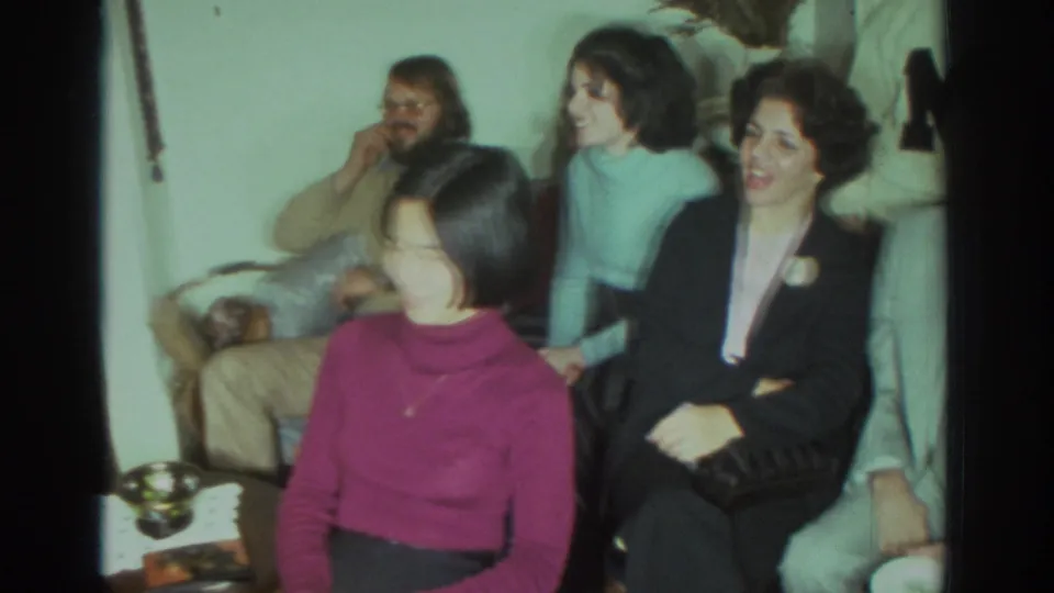 1972 Toronto 8mm frame of adults in a living room reacting to an off-camera speaker or shared activity.