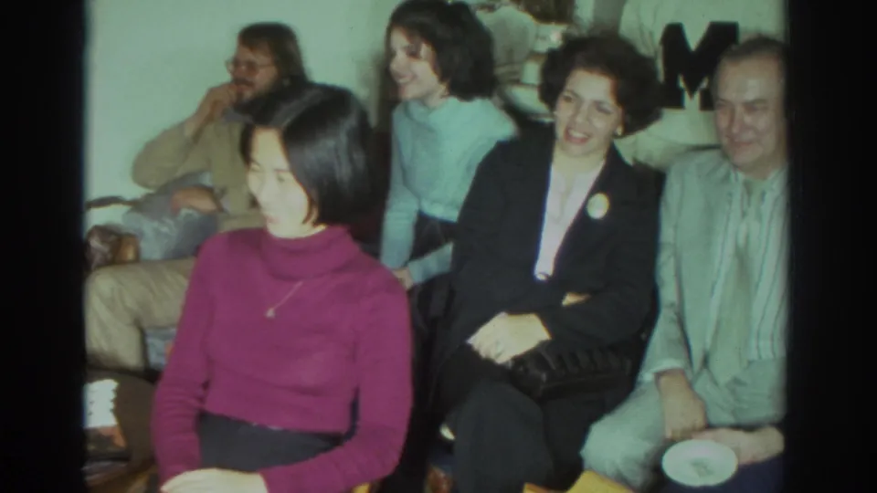 1972 Toronto home-movie frame of seated adults in a private living room, with faces turned toward an off-camera event.