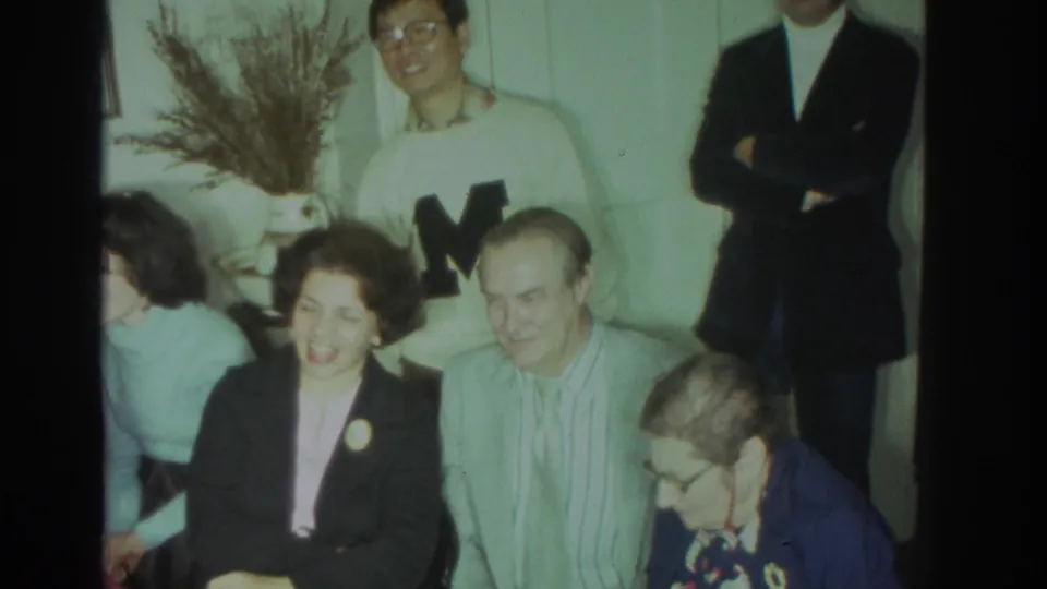 1972 Toronto home-movie view of adults smiling in a private interior, with glasses, jackets, a white lettered sweater, and soft 8mm color.
